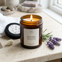 Load image into Gallery viewer, Pure lavender essential oil candle, in an amber glass jar, labeled 'Provence' on a windowsill with lavender flowers and a towel. 
